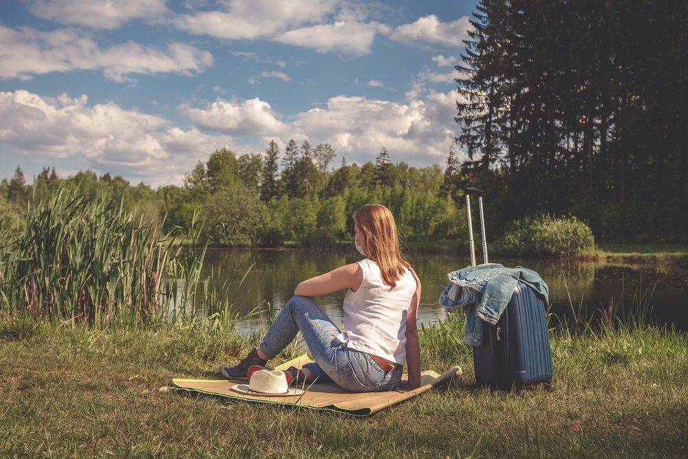 Woman sits on a picnic blanket, next to a WV pond during their staycation. 